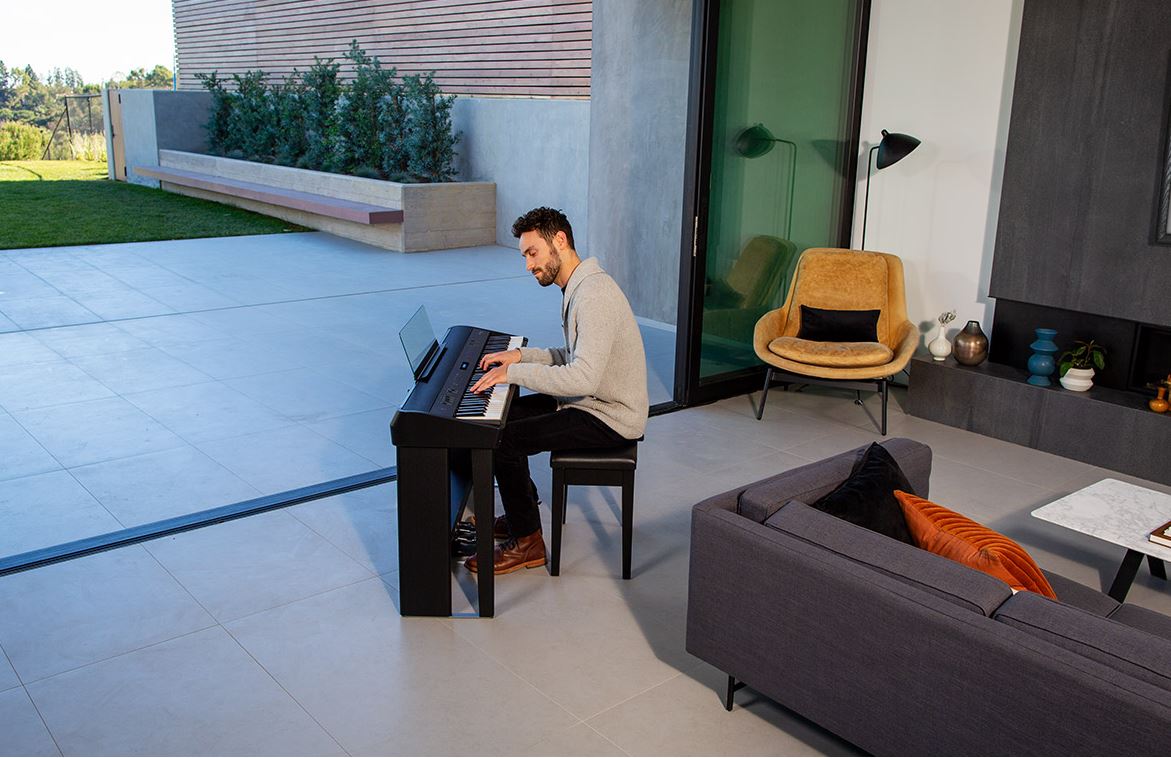 Un homme joue du piano dans son salon avec un grande baie vitrée donnat sur son jardin