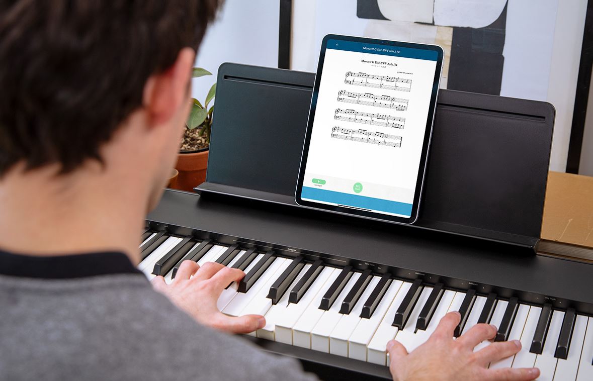 un homme joue du piano en regardant sa partition sur un iPad posé sur un pupitre