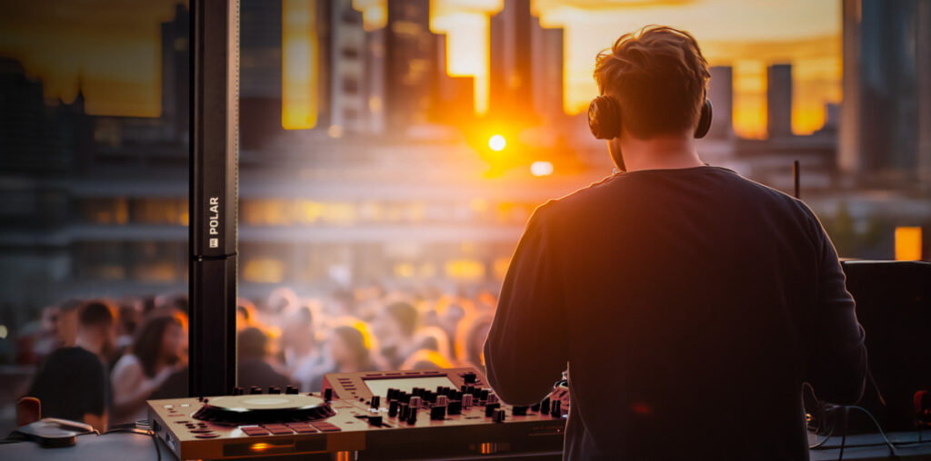 DJ mixant en plein air au coucher du soleil avec une enceinte colonne active HK Audio POLAR, modèle 10 ou 12 MK2, devant un public animé et un décor urbain moderne.