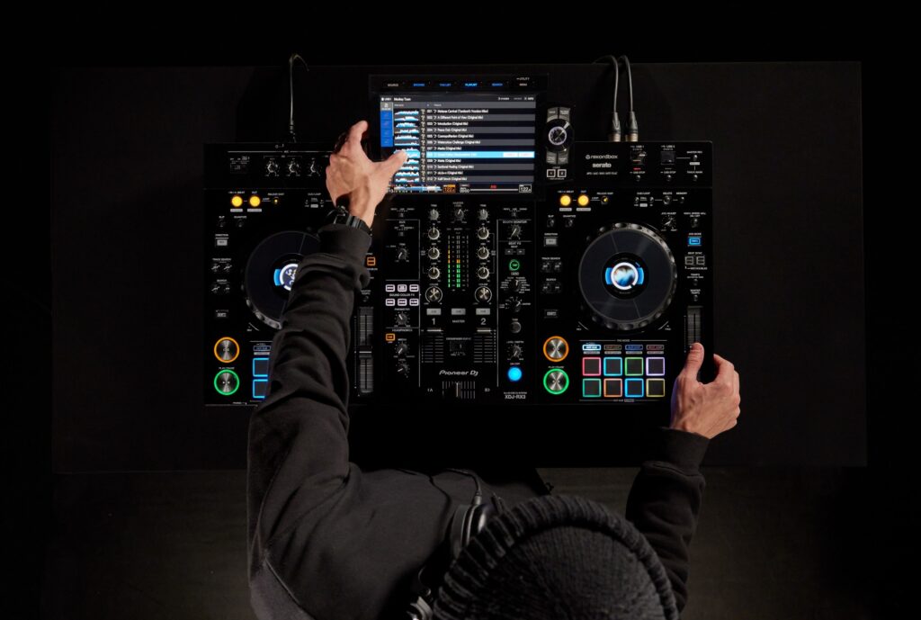 DJ mixant sur un Pioneer DJ XDJ-RX3 vu du dessus, avec écran tactile, jog wheels lumineux et pads de performance, pour comparer ses fonctions avancées au AlphaTheta XDJ-AN
