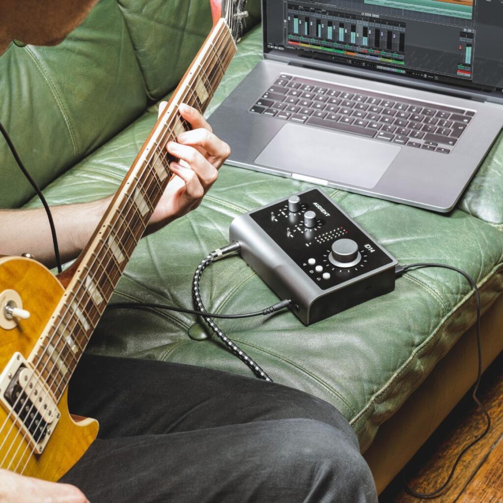 Guitariste branché en entrée instrument sur une interface audio Audient iD14 reliée à un ordinateur portable affichant un logiciel d’enregistrement