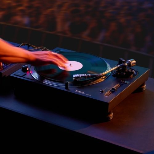 Main de DJ sur un vinyle tournant sur une platine Technics SL-1210MKX en cabine devant le public d’un club